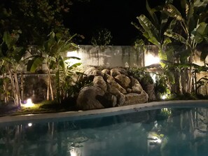 A nighttime pool area with a rock formation and tropical plants. - Solar Água no Centro da Pipa (Tibau do Sul)