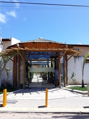 A building entrance with a wooden pergola, glass doors, and a clear sky. - Solar Água no Centro da Pipa (Tibau do Sul)
