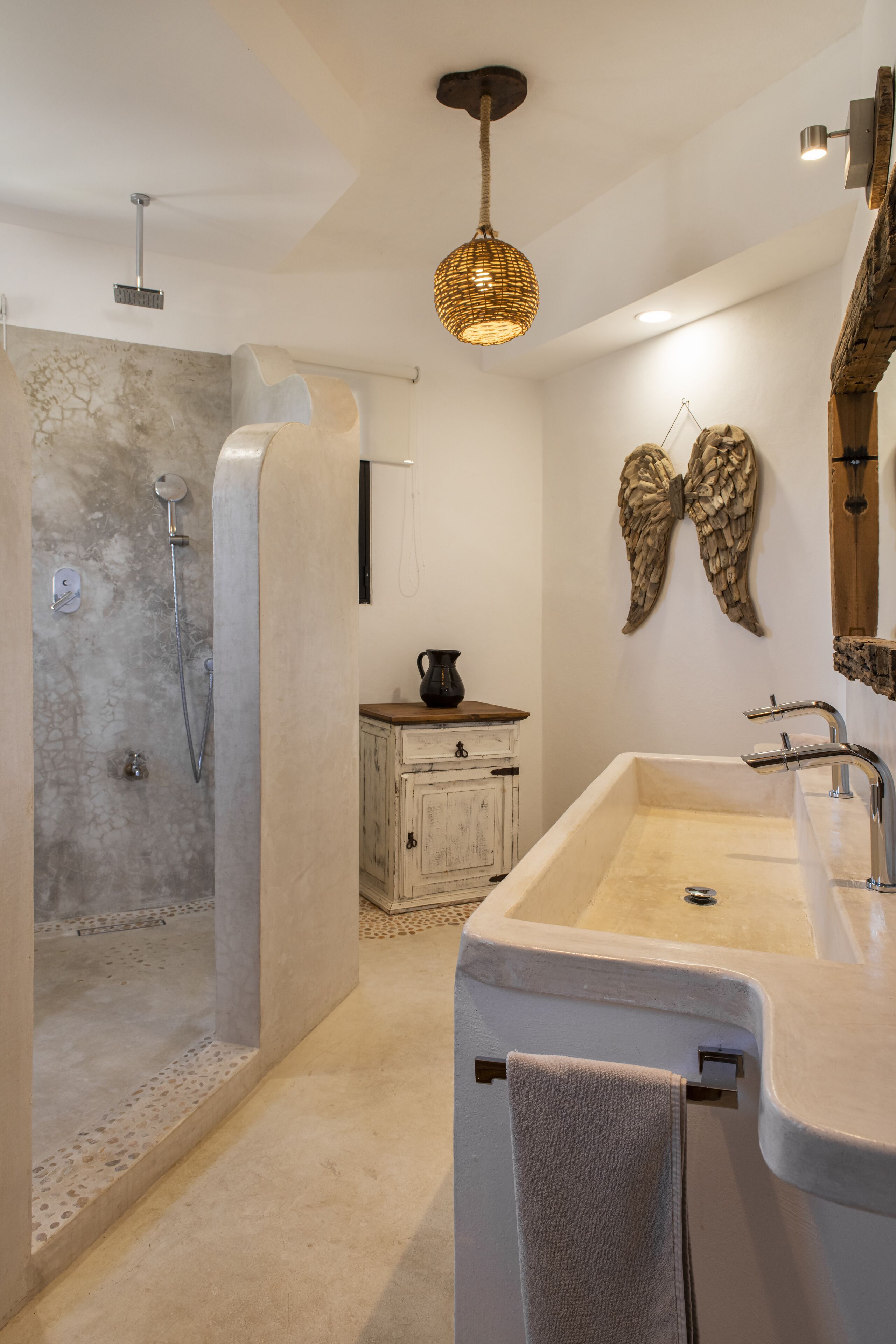 Een moderne badkamer met een douche, wastafel en decoratieve elementen zoals een spiegel in vleugelvorm aan de muur en een geweven lamp.