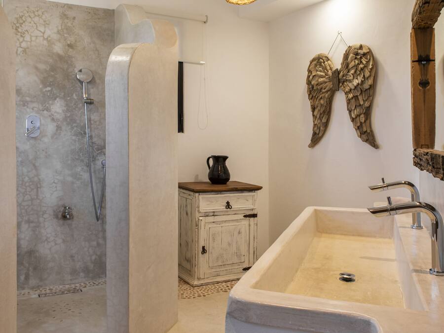 Een moderne badkamer met een douche, wastafel en decoratieve elementen zoals een spiegel in vleugelvorm aan de muur en een geweven lamp.