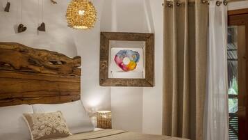 Quarto com cabeceira de madeira, cama com manta bege, obra de arte emoldurada, luminária pendente e janela com cortinas.