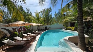 A swimming pool with lounge chairs and umbrellas, surrounded by palm trees. - El Corazón Boutique Hotel - Adults Only with Pool & Beach Club Access (Isla Holbox)