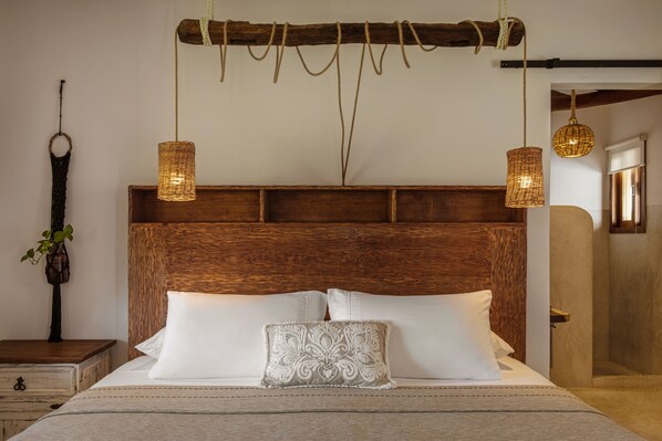 Una cama con cabecera de madera, dos almohadas blancas y una lámpara colgante decorativa.