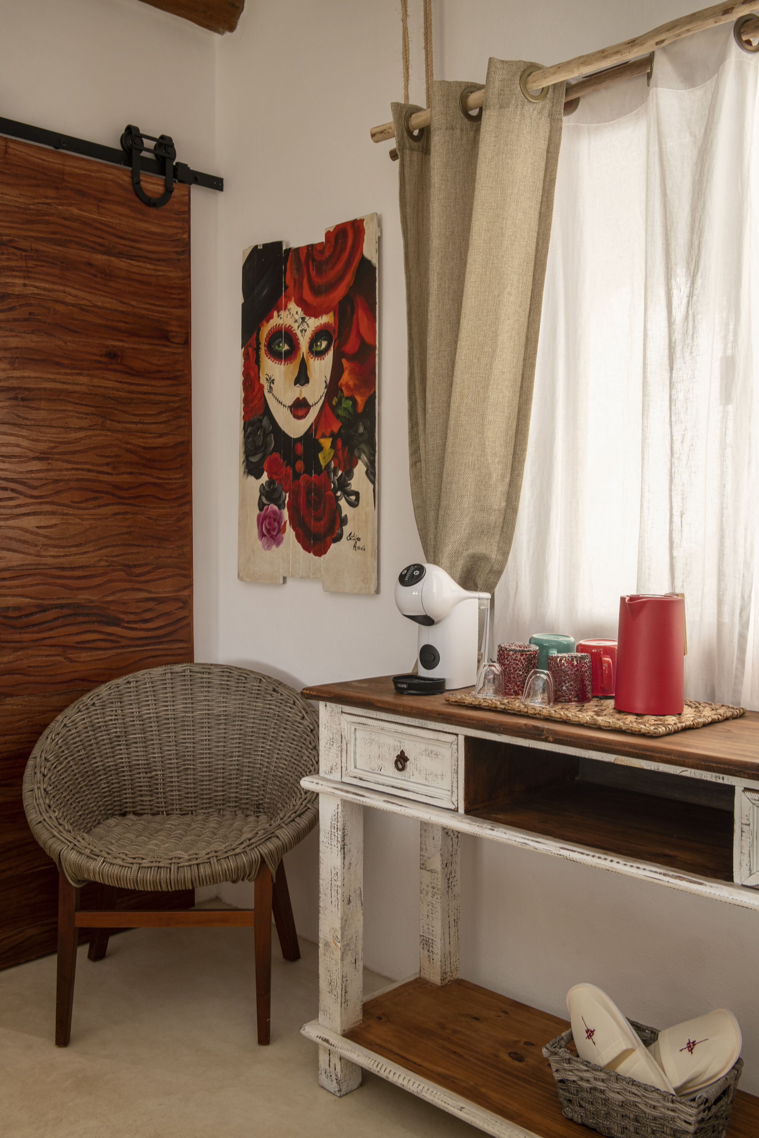 A rustic room with a wooden desk, a wicker chair, a wall-mounted lamp, and a painting.