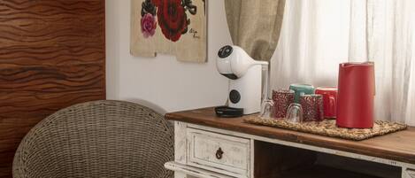A rustic room with a wooden desk, a wicker chair, a wall-mounted lamp, and a painting.