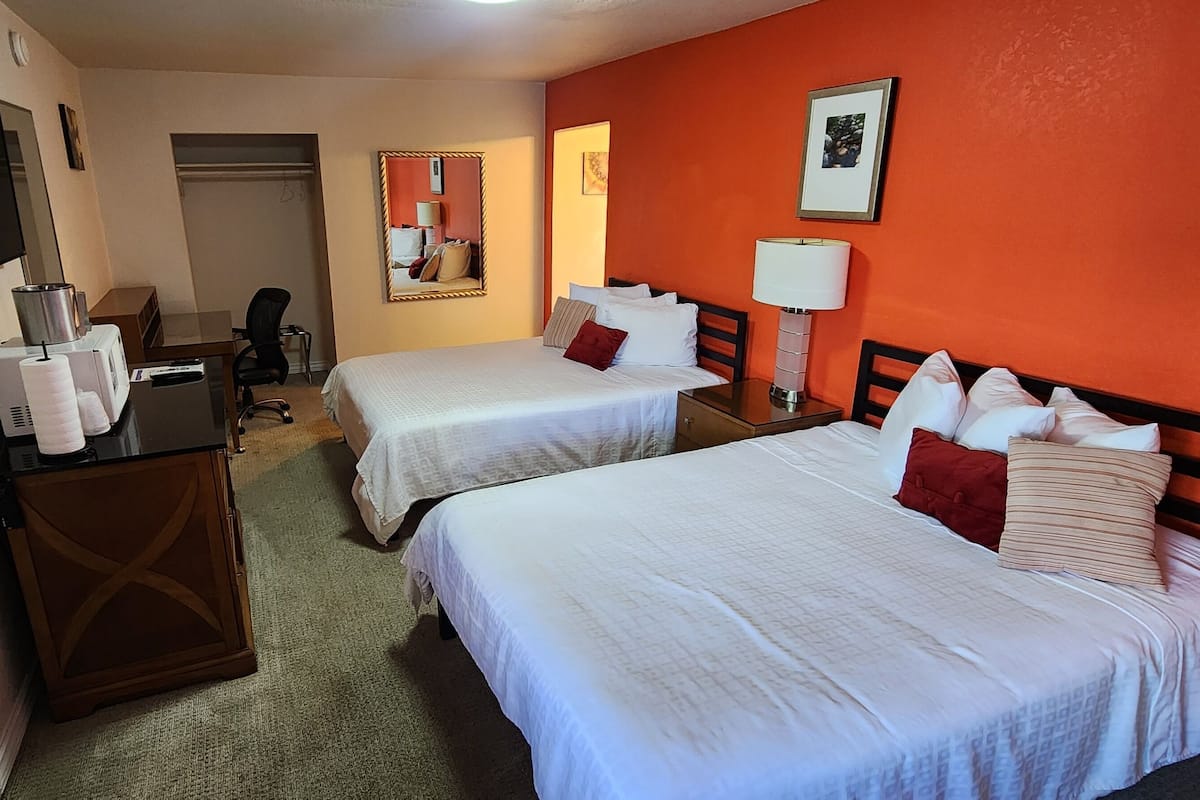 A hotel room with two beds, a desk with a computer, a TV, and a mirror.