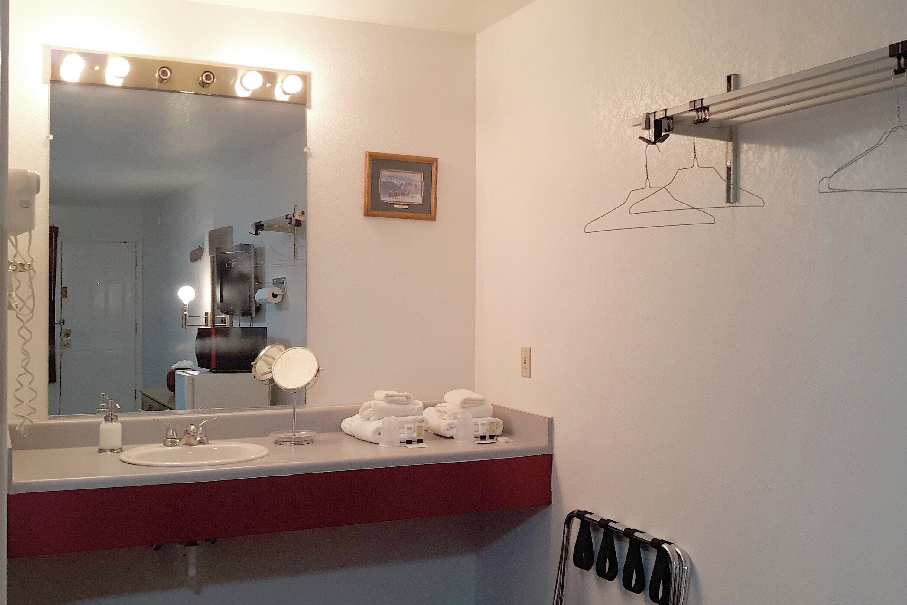 Un baño con un espejo grande, luces, un lavamanos y toallas.