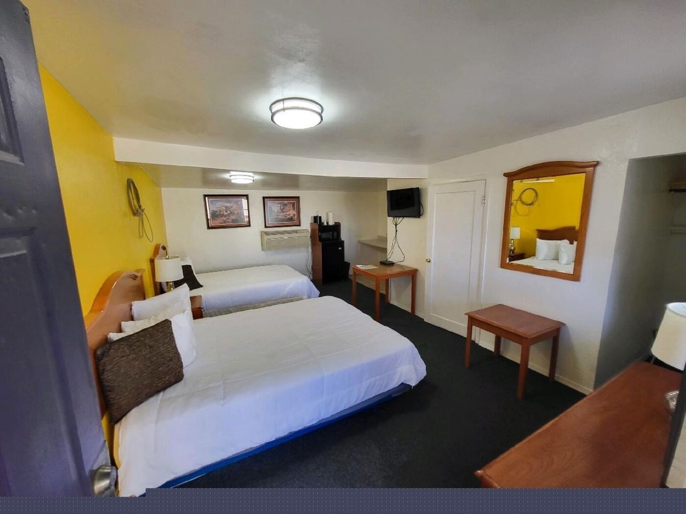 A hotel room with two beds, a desk, a chair, a TV, and a mirror.