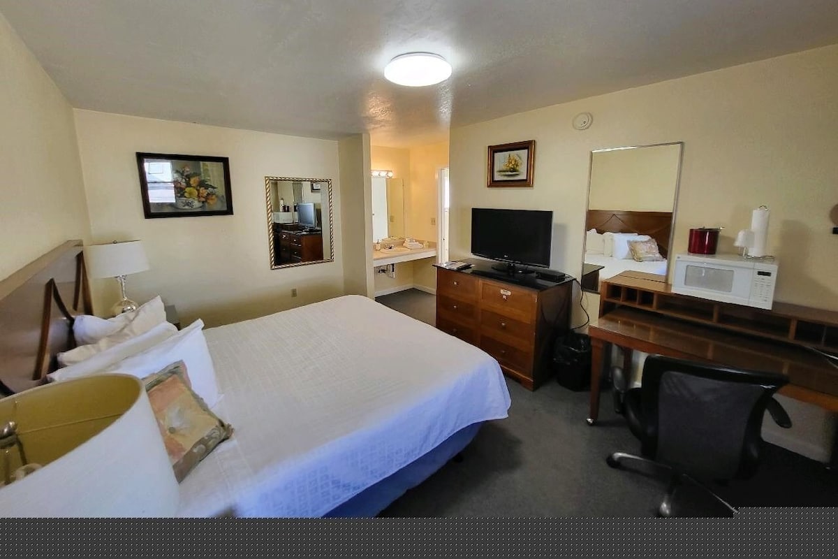 A hotel room with a bed, a desk, a television, a microwave, a chair, and a dresser.