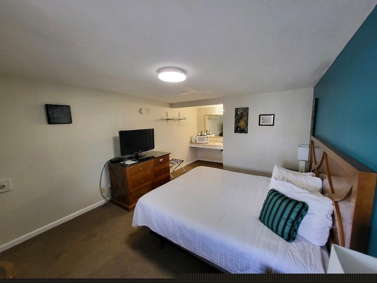 A hotel room with a bed, a dresser, a television, and a bathroom visible in the background.