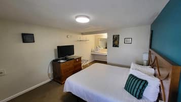 A hotel room with a bed, a dresser, a television, and a bathroom visible in the background.