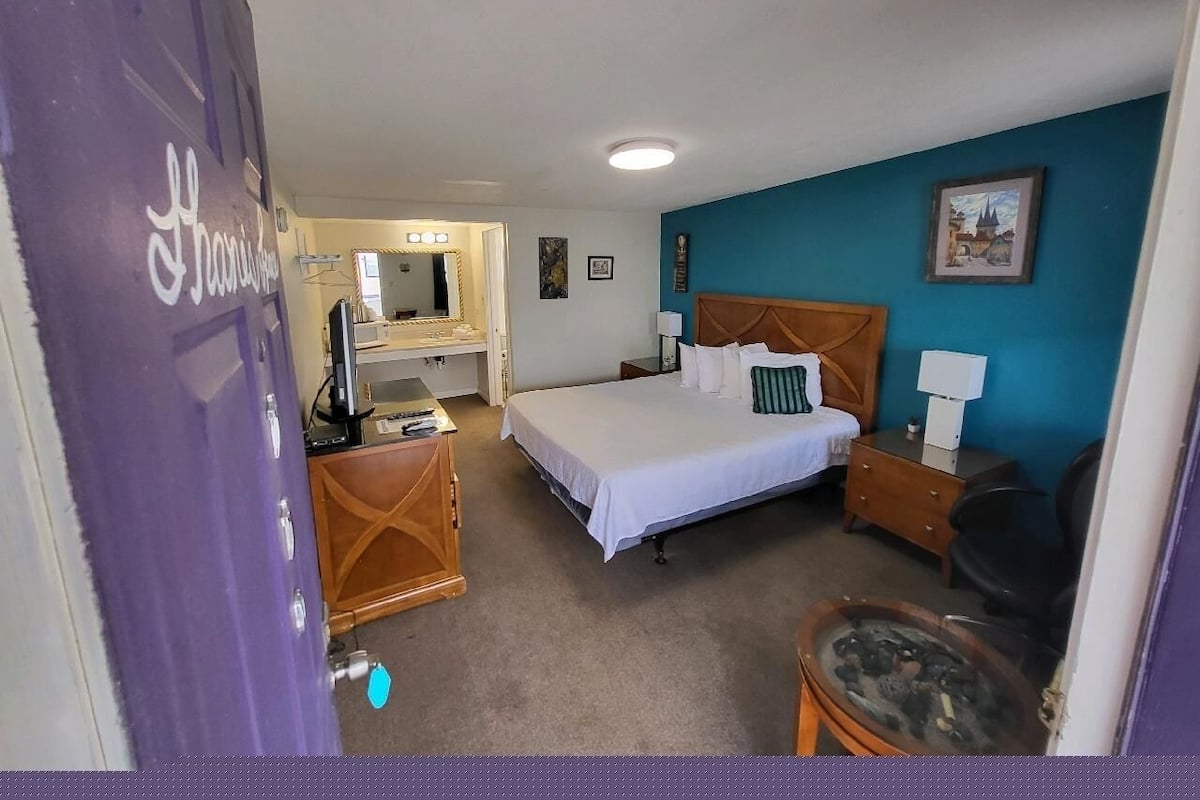 A hotel room with a bed, a desk, a chair, a dresser, and a mirror.