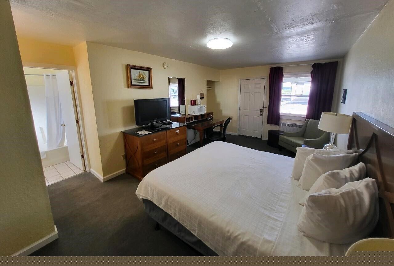 Een hotelkamer met een bed, een bureau, een stoel, een televisie en een raam met gordijnen.