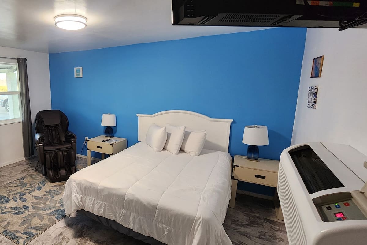 A hotel room with a bed, a massage chair, a heater, and a window with curtains.