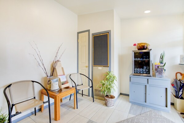 A reception area with a wooden desk, two chairs, a potted plant, a blue cabinet with a decorative item on top, and a door with a screen.