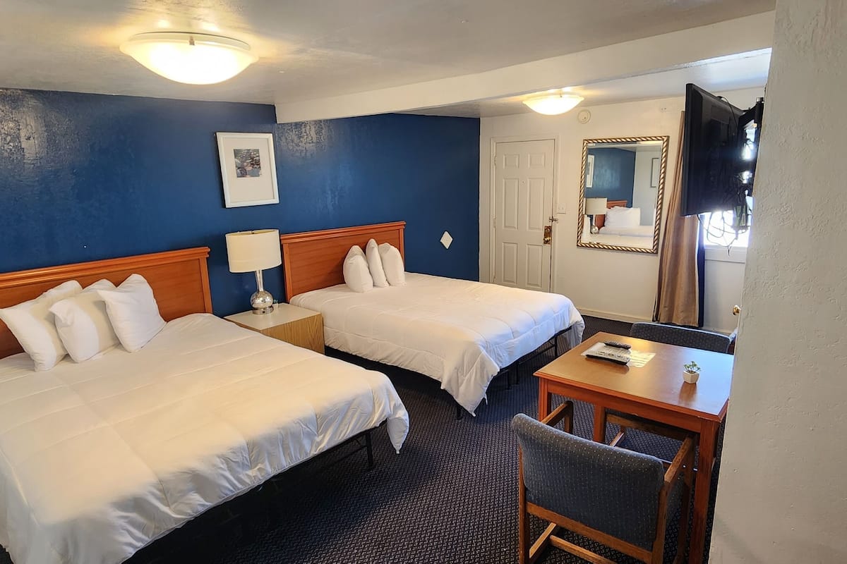 A hotel room with two beds, a desk, a chair, a lamp, a TV, and a mirror.