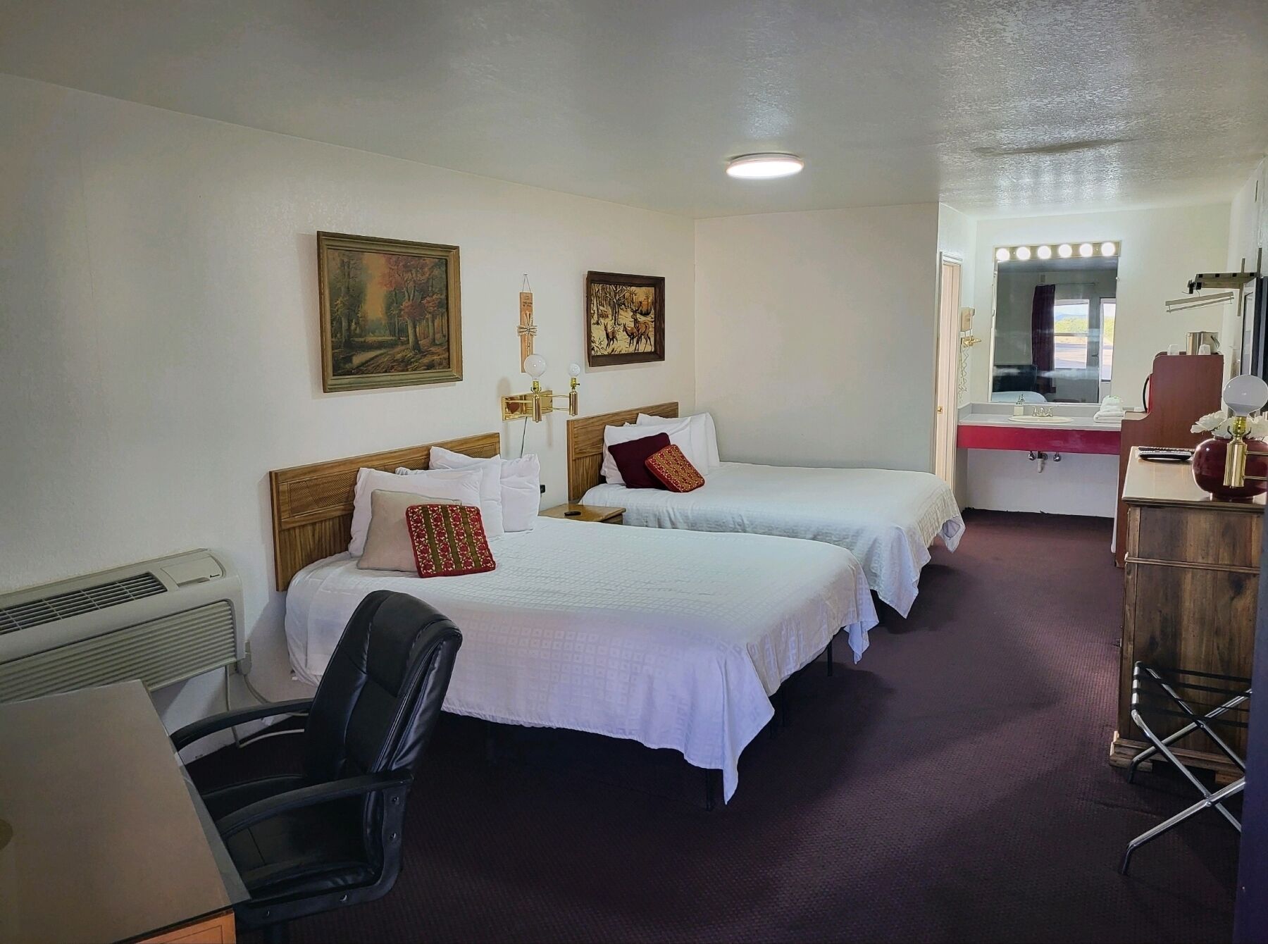 A hotel room with two beds, a desk with a mirror, a chair, and a vanity with a mirror.