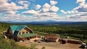 A log cabin with a green roof, surrounded by a forest and mountains in the background. - Alpine Creek Lodge (Cantwell)