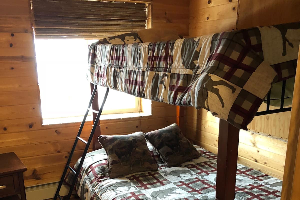Un lit superposé avec une couverture à carreaux, une échelle en bois et une petite table en bois.
