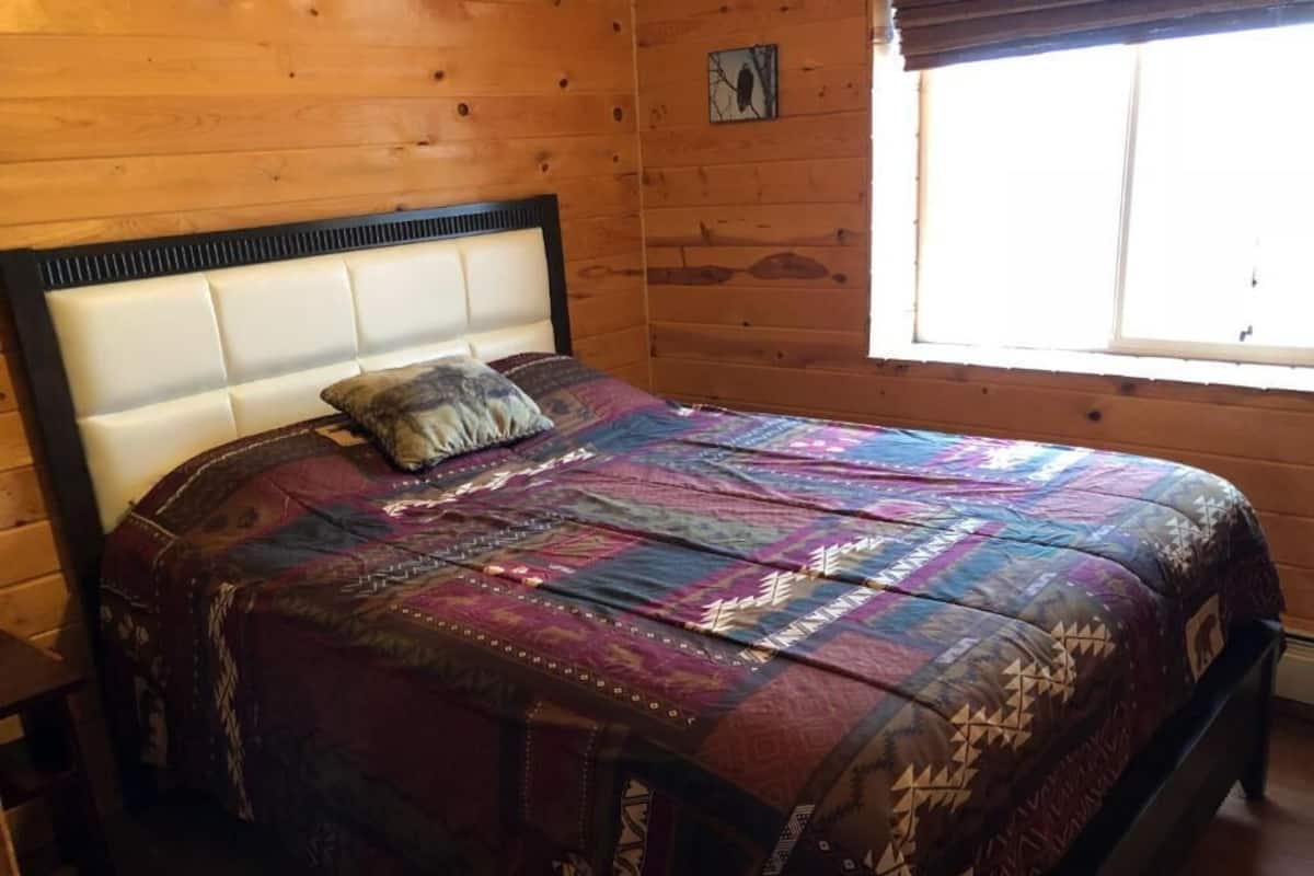 Une chambre dans un chalet en bois, avec un lit recouvert d’une courtepointe à motifs.