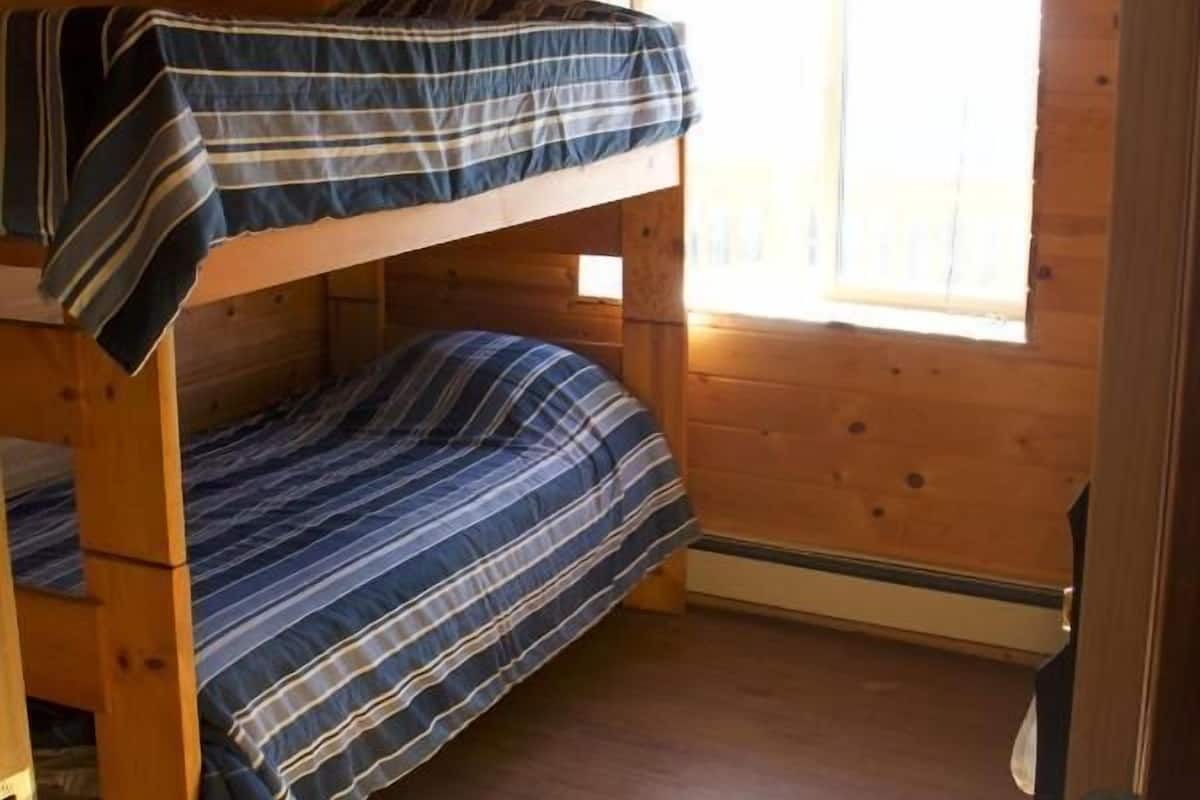Une chambre avec des lits superposés, des murs en bois et une fenêtre avec des stores.