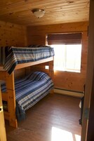 Habitación con literas, paredes de madera y una ventana con persianas.