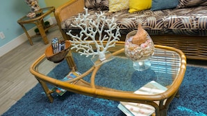 A glass-top coffee table with a woven base, surrounded by a blue shag rug. - Jubilee Gardens Freeport (Freeport)