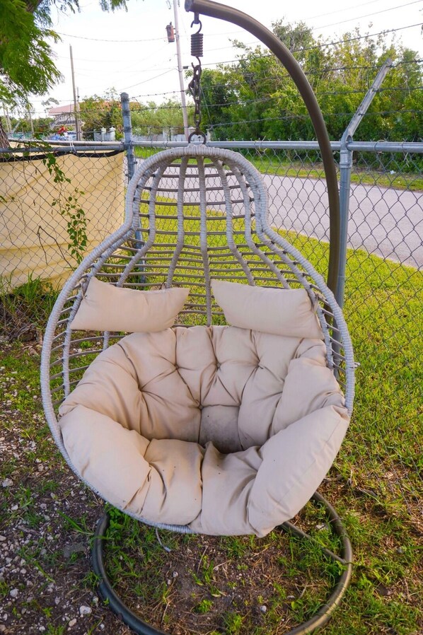 A hanging chair with a cushioned seat and backrest, suspended by a metal frame and chain. - Jubilee Gardens Freeport (Freeport)
