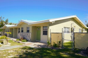 A single-story house with a green door, a stone wall, and a fenced yard. - Jubilee Gardens Freeport (Freeport)