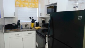 A kitchen with white cabinets, a black refrigerator, a microwave, and a coffee maker. - Jubilee Gardens Freeport (Freeport)