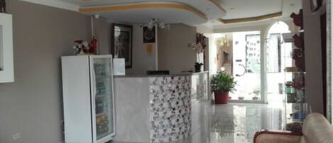 A modern living room with a beige sofa, a white refrigerator, and a tiled backsplash in the kitchen area.