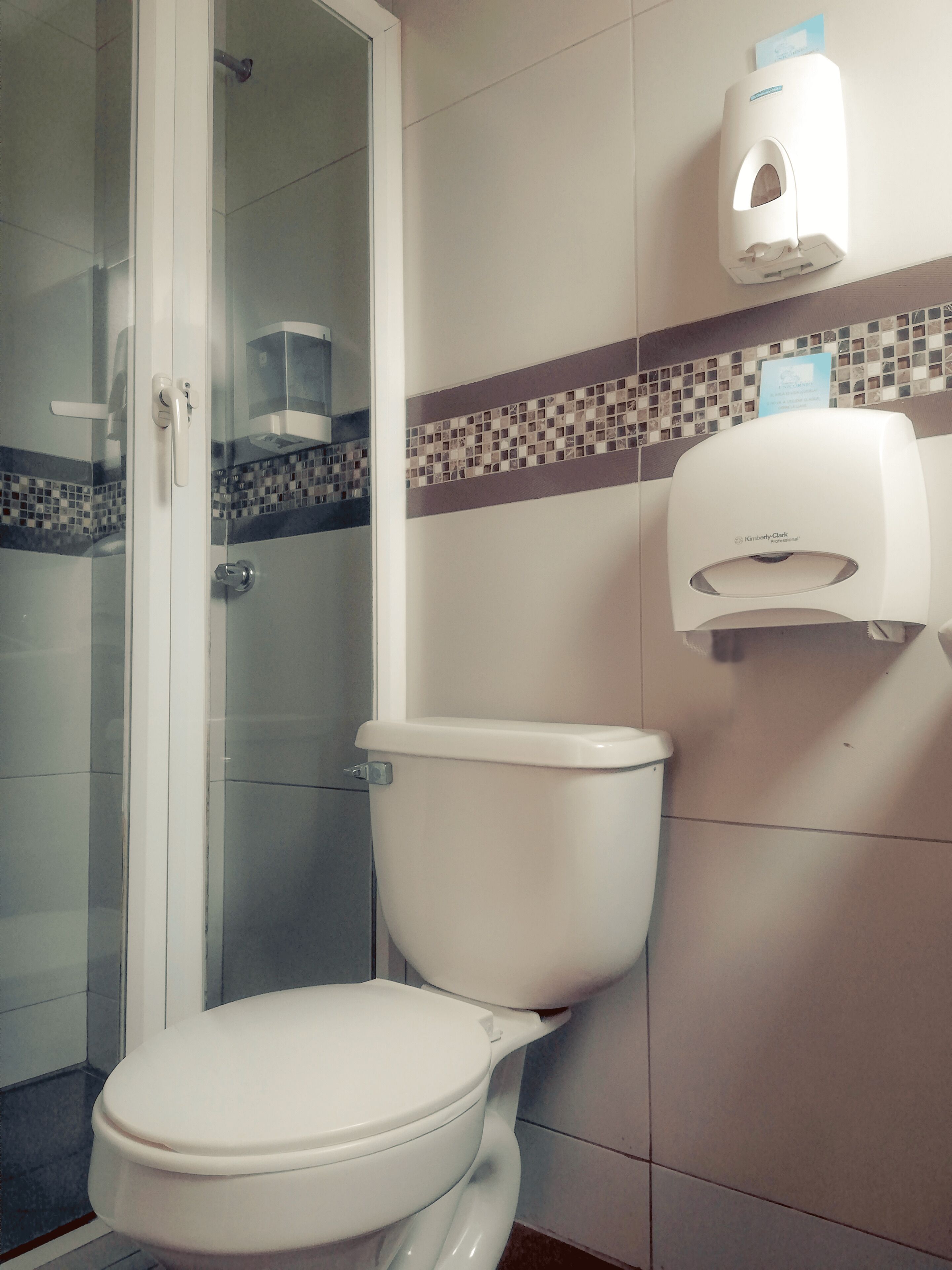 A bathroom with a toilet, a glass shower enclosure, and a hand sanitizer dispenser.