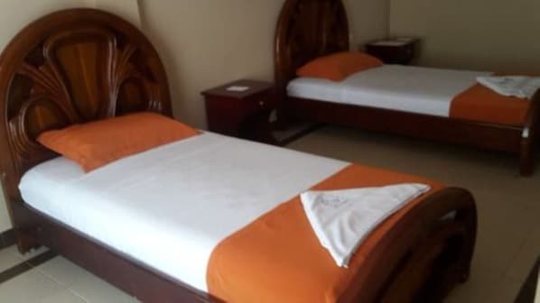 Dos camas de madera con ropa de cama blanca y naranja, una mesita de noche y un estante en la pared.
