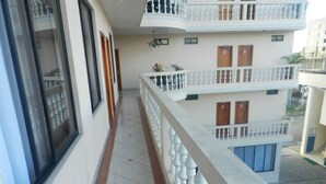 A narrow balcony with white balustrades, a tiled floor, and a view of a multi-story building with balconies and windows. - Hotel Unicornio (Coca)