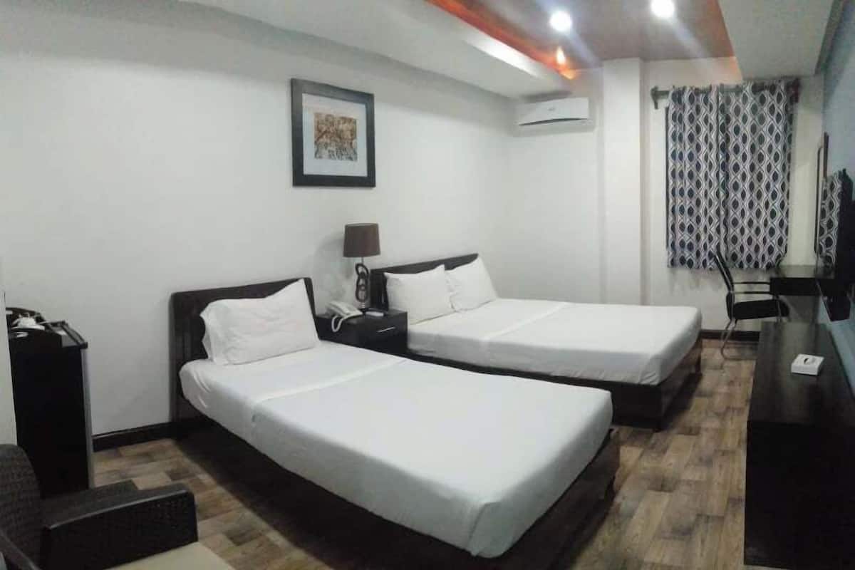 Quarto de hotel com duas camas de solteiro, uma escrivaninha, uma cadeira e um ar condicionado.