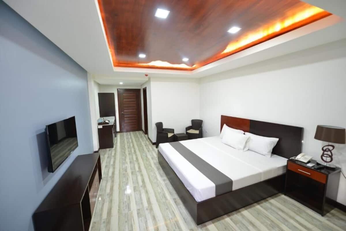 Quarto de hotel moderno com uma cama grande, televisão de tela plana, escrivaninha e uma cadeira.