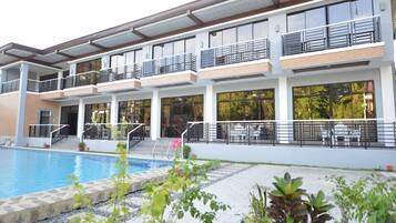 A modern hotel with a swimming pool, multiple balconies, and outdoor seating areas.