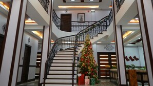 Een ruime lobby met een imposante trap, een groot houten plafonddecor en een versierde kerstboom.