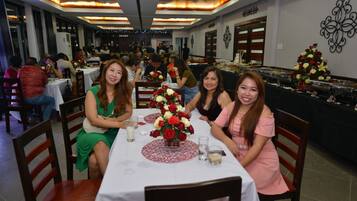 A restaurant with multiple tables, some with floral centerpieces, and a buffet area in the background.