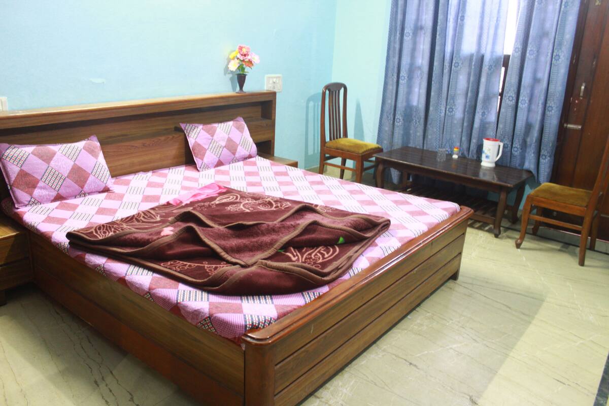 Een slaapkamer met een bed, een houten nachtkastje, een bureau en een stoel.