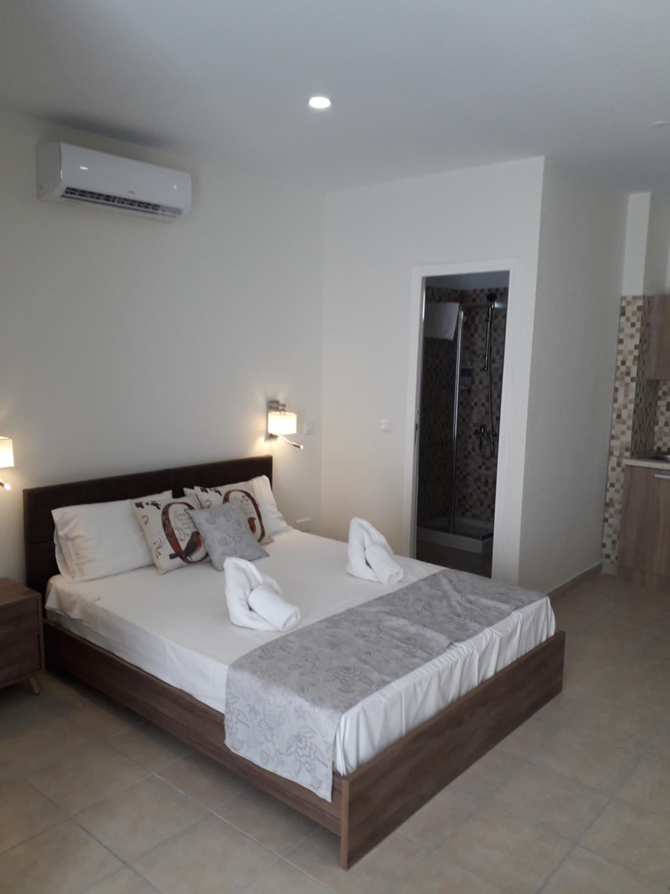 Una cama bien hecha con ropa blanca y toallas, un cabecero de madera y un aire acondicionado instalado en la pared.