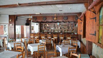 Un restaurante con mesas y sillas de madera, una zona de bar con estantes llenos de botellas y una pared de ladrillo.