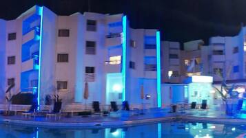 Un edificio moderno con zona de piscina, incluyendo sillones de descanso y una piscina.