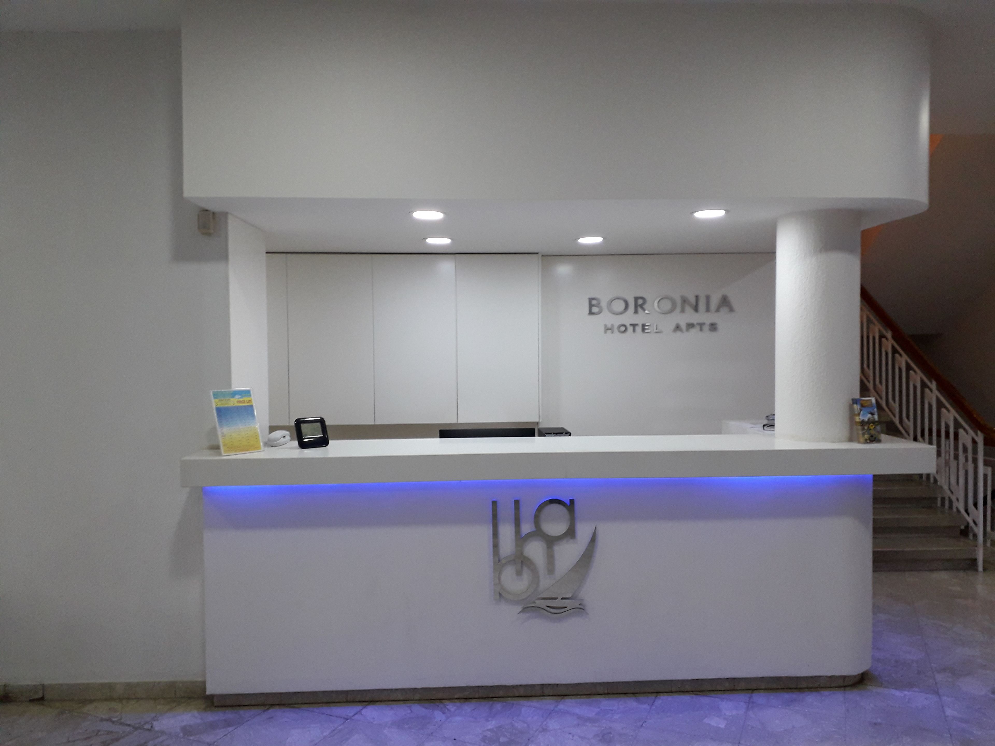 Un mostrador de recepción de diseño moderno, con el logotipo y el nombre 'BORONIA HOTEL APTS'.