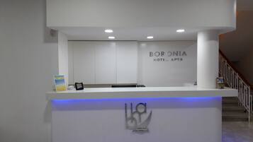 Un mostrador de recepción de diseño moderno, con el logotipo y el nombre 'BORONIA HOTEL APTS'.