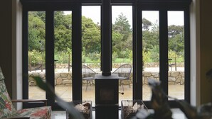 A room with a large window, a fireplace, and outdoor seating. - Te Arai Lodge (Te Arai)