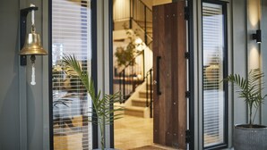 A modern entrance with a wooden door, a bell, and potted plants. - Te Arai Lodge (Te Arai)