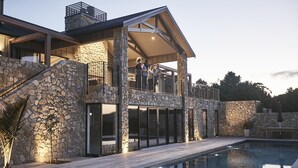 A modern house with a stone facade, a pool, and a covered outdoor area. - Te Arai Lodge (Te Arai)