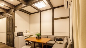 A compact kitchen with a microwave, sink, and a small refrigerator. There is a wooden table with stools and a grey sofa with cushions. - JINYA Fujikawaguchiko (Fujikawaguchiko)