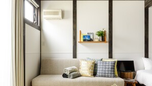 A room with a sofa, a small table with a tray, a bed, a shelf with books and a plant, and a window with curtains. - JINYA Fujikawaguchiko (Fujikawaguchiko)